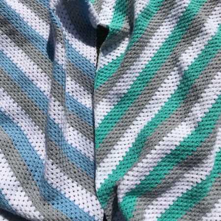 Close up of granny stitch crochet blankets in grey, white, blue and green