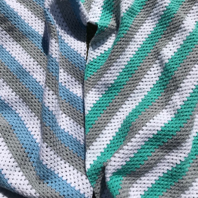 Close up of granny stitch crochet blankets in grey, white, blue and green